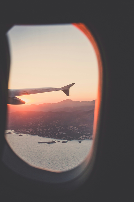View from an airplane window showing the wing and a scenic sunset over mountains and the sea, highlighting the convenience of staying online with an eSIM while traveling.