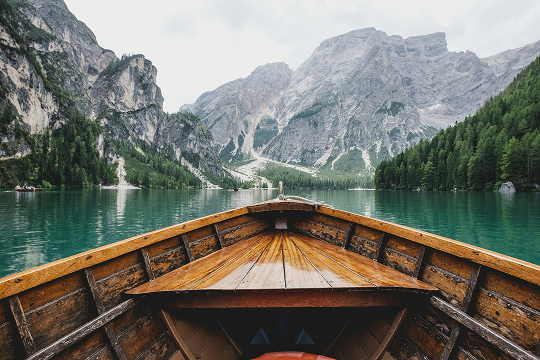Wooden boat on a crystal-clear lake surrounded by mountains and lush greenery, highlighting the convenience of using an eSIM for uninterrupted connectivity during travel.